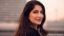 Portrait of DW Waslat Hasrat-Nazimi. She is standing sideways while looking and smiling directly at the camera. Her long dark hair is loose and she wears dark brown lipstick. 
