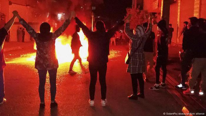 Menschen stehen in einem Kreis um ein Feuer auf der Straße und halten sich an den Händen. 