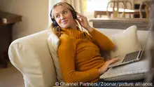 Smiling caucasian woman relaxing on couch in living room wearing headphones and using laptop. spending free time at home with technology. || Modellfreigabe vorhanden