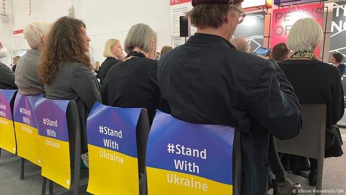 Blick auf Stuhllehnen, die mit Plakaten behängt sind, auf denen steht: Stand with Ukraine.
