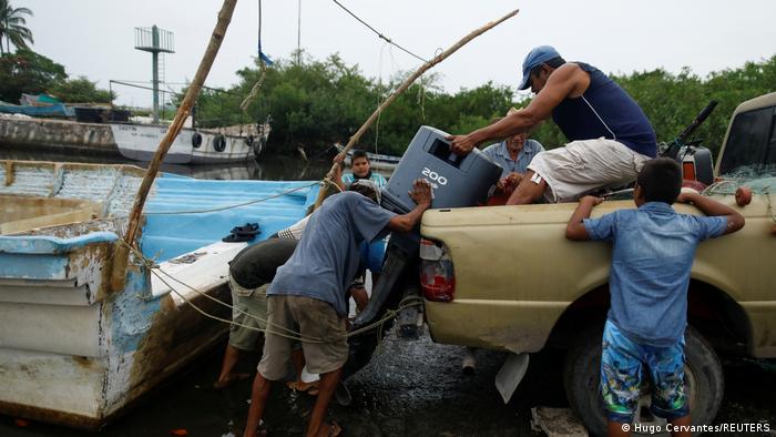 Varias personas cargan un vehículo entre barcos de pescadores.