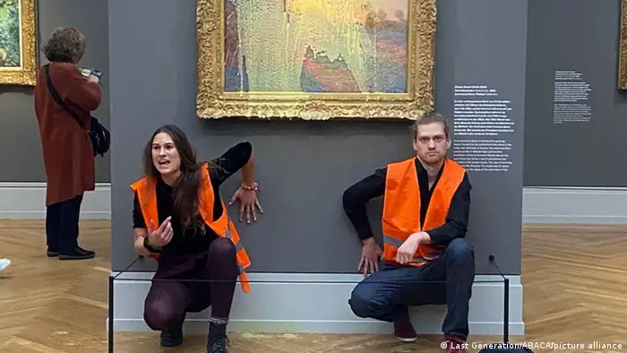 Zwei junge Leute in Warnwesten knien vor einem Gemälde, das mit Kartoffelpüree besprüht wurde.