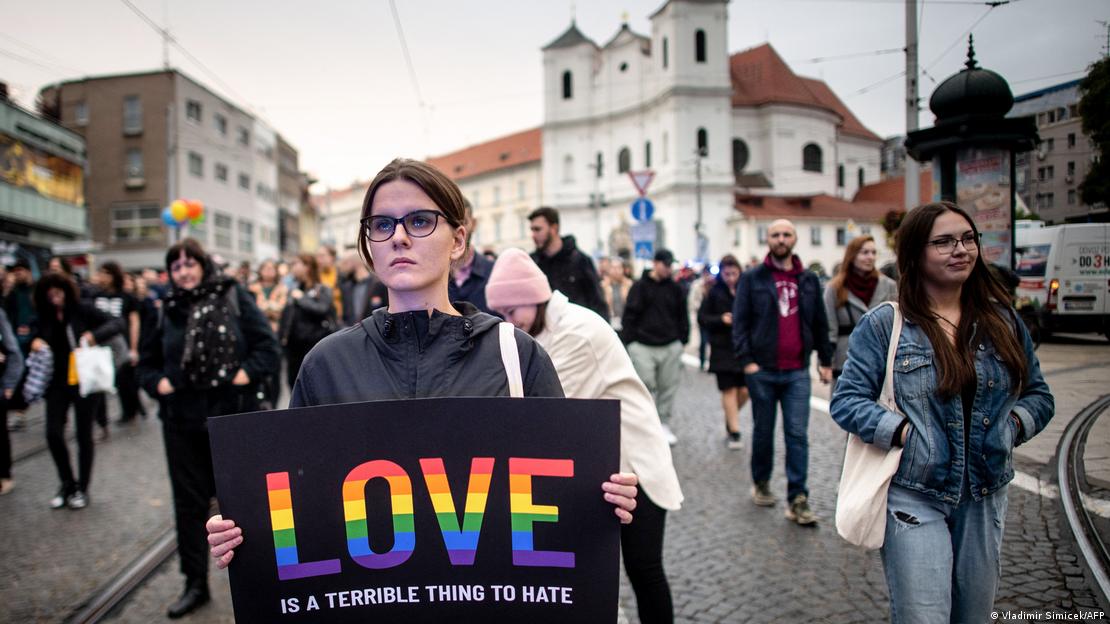 Eine junge Frau mit Brille hält ein T-Shirt in den Händen mit der Aufschrift: "LOVE IS A TERRIBLE THING TO HATE"