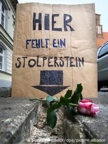 Plakat: Hier fehlt ein Stolperstein auf einer beschädigten Gehplatte Plakat: Hier fehlt ein Stolperstein auf einer beschädigten Gehplatte