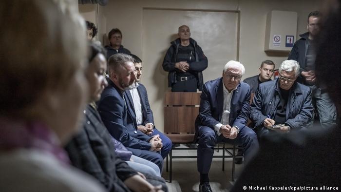 Frank-Walter Steinmeier gemeinsam mit Zivilisten aus Korjukiwka im Luftschutzbunker, auf Stühlen sitzend