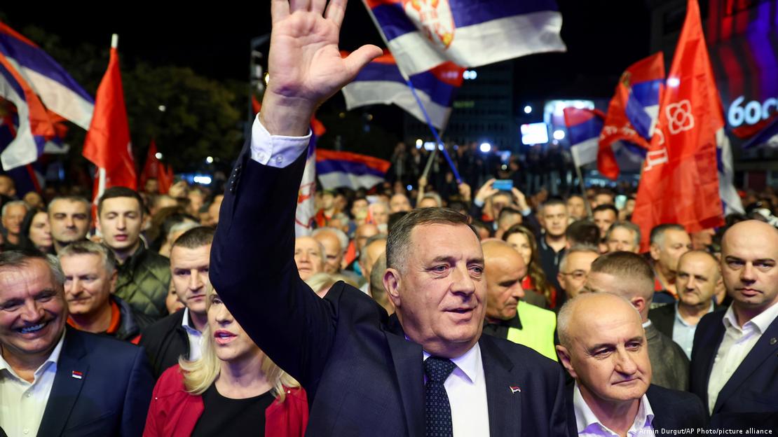 Milorad Dodik kalabalık bir mitingde destek&ccedil;ilerinin arasında elini kaldırıyor; &ccedil;evresinde Sırp Cumhuriyeti bayrakları taşıyan kişiler var