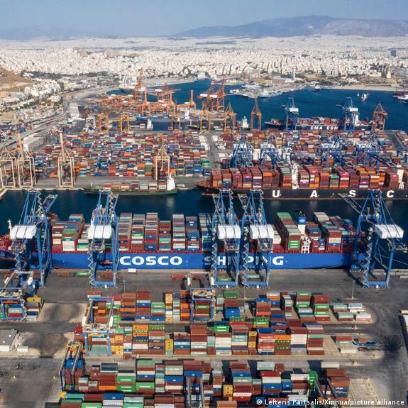 Aerial view of a Cosco cargo ship moored between two piers covered with colorful shipping containers.