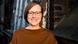 Journalism Professor Christina Elmer smiles into the camera. In the head shot, she wears a light brown sweatshirt and dark-framed glasses.