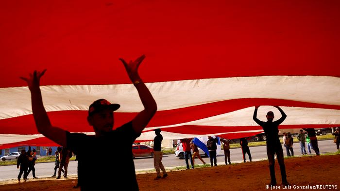 Migrantes venezolanos llevan una gran pancarta que se asemeja a la bandera de Estados Unidos, un proyecto del artista mexicoestadounidense Roberto Márquez, también conocido como Robenz, durante una protesta contra las nuevas políticas contra la migración del gobierno de Joe Biden, en un campamento cerca de las orillas del río Bravo, en Ciudad Juárez, México.