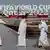Vier Männer in weißen Gewändern spazieren vor dem Schriftzug der FIFA Fußball-Weltmeisterschaft Katar 2022
