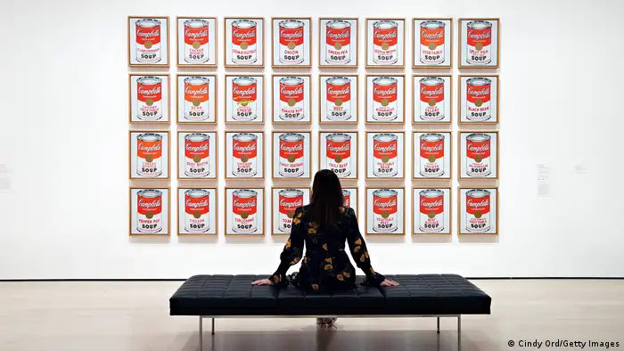 Eine Person sitzt vor Andy Warhols Kunstwerk Campbell's Soup Cans.