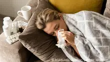 Sick woman with a runny nose symptom lying under the blanket at home || Modellfreigabe vorhanden