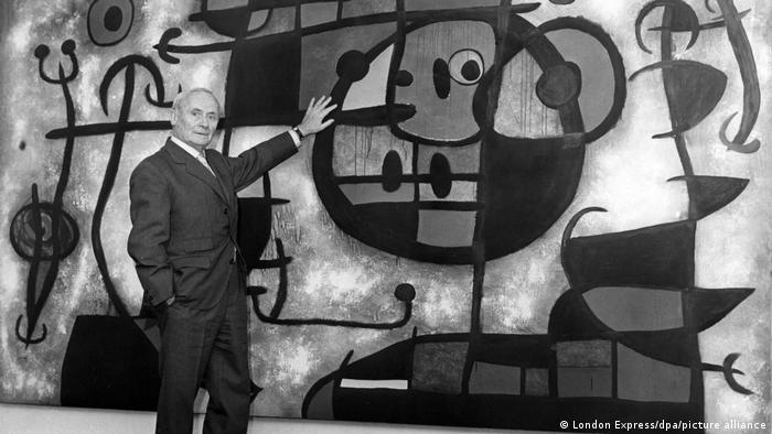 Joan Miró vor einem seiner Werke gestikulierend.