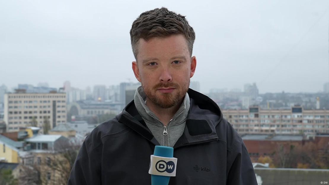 DW reporter Nick Connolly, man holding a DW microphone in front of a cityscape  