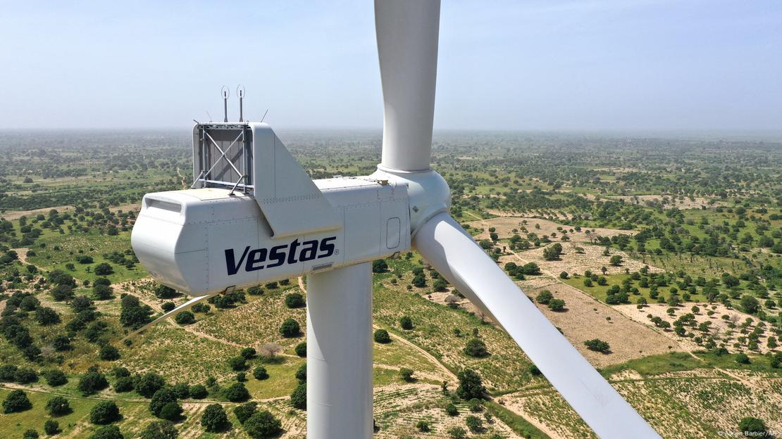 A wind turbine in Senegal stands against a landscape of trees and fields