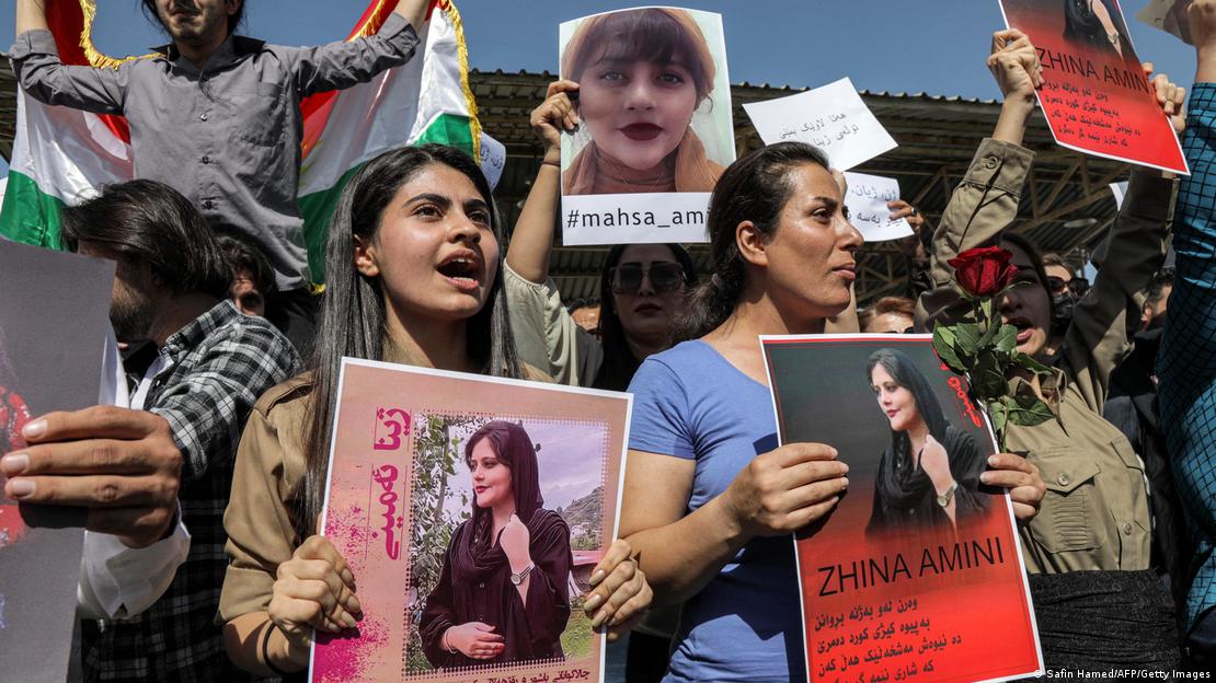 Women, not wearing hijabs, holding posters with the image of Mahsa Amini and shouting
