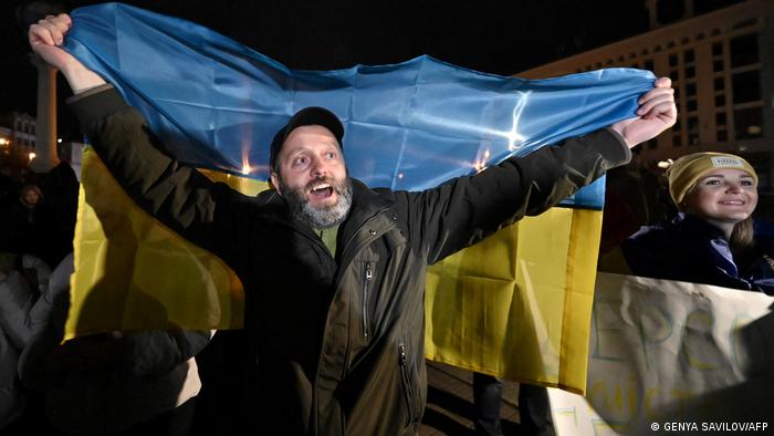 Un hombre grita entre la multitud alzando una bandera ucraniana.