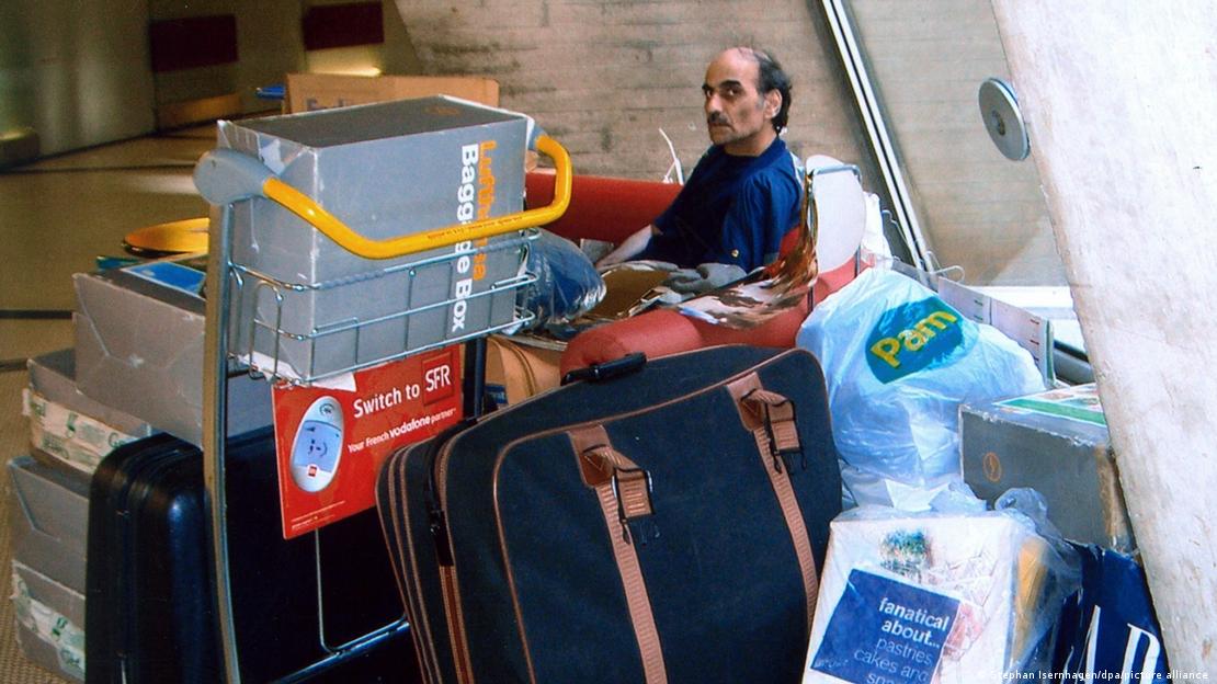 Mehran Karimi Nasseri no aeroporto internacional de Paris, em 2004, sentado em um banco e reoedado de sacolas plásticas, caixas e malas