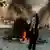 Mulher com véu islâmico levanta o punho diante de uma fogueira no meio da rua