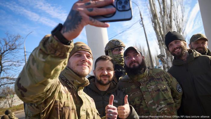 Soldaten und ein Mann im olivfarbenen Anorak machen Selfies und halten die Daumen hoch