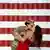 Delante de la imagen de la bandera estadounidense, una soldado besa a su esposa. 