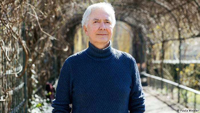 Autor Andreas Isenschmid steht in einem bepflanzten Durchgang. Er trägt einen blauen Rollkragenpullover.