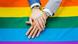 One person's hand on top of another person's hand on a rainbow flag One person's hand on top of another person's hand on a rainbow flag
