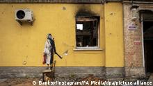 Sprüh-Bild an der Fassade eines ausgebranntes Hauses zeigt eine Frau mit Lockenwickler, Gasmaske, einem Morgenmantel und einen Feuerlöscher in der Hand