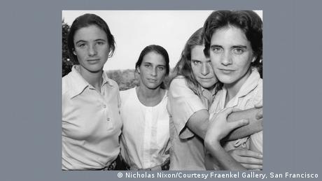 Schwarz-weiß-Fotografie der vier Brown Sisters. In weißen Blusen stehen sie nebeneinander und lächeln in die Kamera.