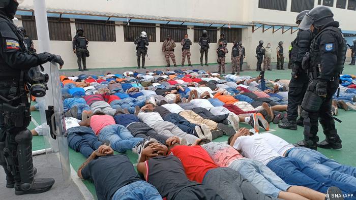Foto de agentes de la Policía que observan a decenas de presos maniatados y tirados en el piso.