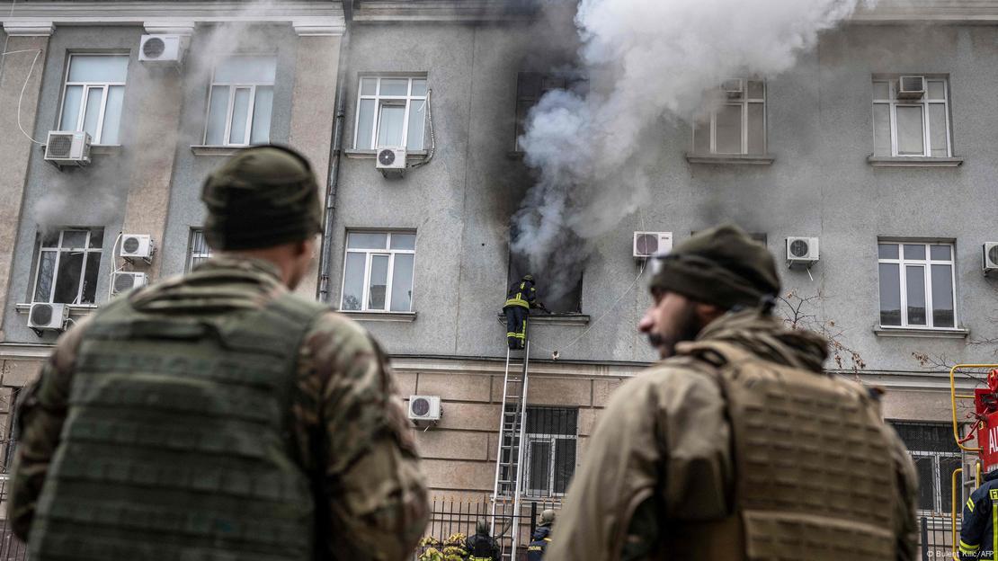 Soldados ucranianos parados enquanto bombeiros extinguem um incêndio em um prédio depois que uma mina deixada pelas forças russas explodiu no centro de Cherson em 18 de novembro de 2022.