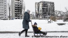 Eine Frau schiebt einen Schlitten mit einem Jungen im Schnee vor zerstörten Hochhäusern