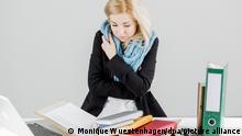 Eine Frau sitzt vor Ordnern am Schreibtisch. Sie hat einen Schal um und die Arme um den Körper geschlungen (Quelle: Monique Wuestenhagen/dpa/picture alliance)