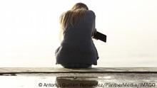 Sad girl holding phone complaining sitting on a ledge