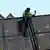 Ein Arbeiter in Kletterausrüstung sichert Container eines havarierten Schiffes