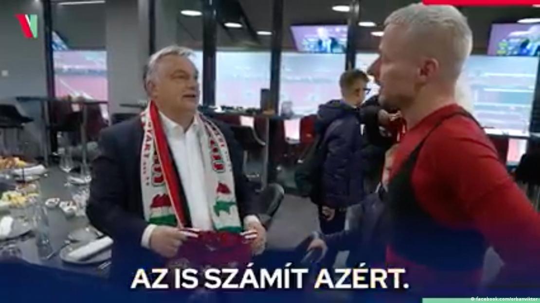 Still from a video on Viktor Orban's Facebook page showing him talking to a member of the Hungarian soccer team and wearing a scarf showing 'Greater Hungary'