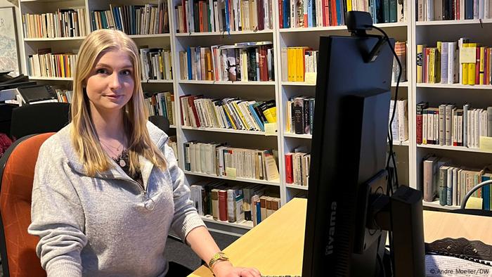 DAG-Mitarbeiterin Charlyn Evert sitzt am Schreibtisch, hinter ihr eine Bücherwand 