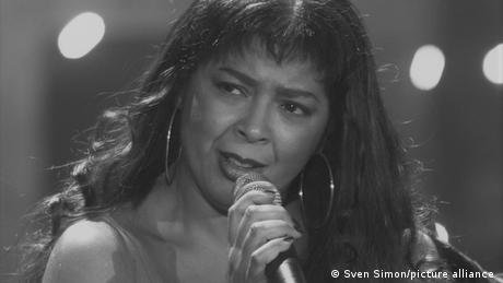 Schwarz-weiß- Foto der Sängerin Irene Cara mit Mikrofon in der Hand 