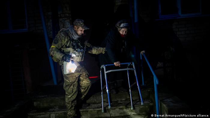 Un soldado ucraniano ayuda en medio de la oscuridad a una mujer.