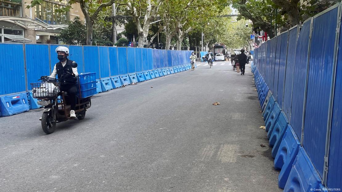 Pessoa dirige moto em rua, com cercas móveis azuis dos dois lados