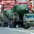 Massive ballistic missiles on a line of dark green military vehicles at a Russian military parade, red buildings in the background