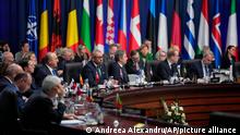 NATO-Außenmister am runden Tisch mit Flaggen im Hintergrund beim NATO-Außenministertreffen in Bukarest, Rumänien