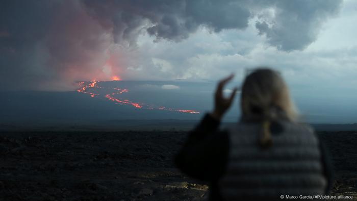 Una donna osserva l'eruzione del Mauna Loa da una distanza di sicurezza.  Sebbene al momento non vi sia alcun pericolo per le città circostanti, sono stati aperti rifugi a Kailua-Kona e Pahala, ha affermato la Protezione civile.
