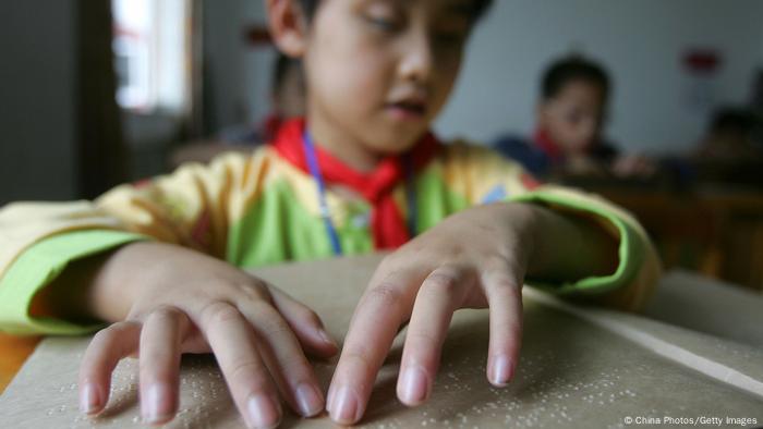 Ein blindes Kind in China tastet mit den Fingern auf einer Braille Tastatur 
