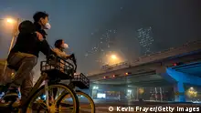 BEIJING, CHINA - NOVEMBER 20: A couple wear protective masks to protect against the spread of COVID-19 as they stop on their shared bikes to look up at the CCTV building obscured by smog and fog on November 20, 2022 on a polluted day in Beijing, China. In an effort to try to bring rising cases under control, the local government closed many restaurants for inside dining, switched schools to online studies, and asked people to work from home. Though the government recently revised its COVID strategy, it has said it will continue to stick to its strict zero tolerance policy with mandatory testings, quarantines and lockdowns in many areas in an effort to control the spread of the virus. (Photo by Kevin Frayer/Getty Images)
