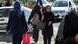 Mulher iraniana atravessando uma rua sem ter a cabeça coberta por lenço. Outra mulher, com lenço na cabeça, atravessa a rua na direção contrária. Mulher iraniana atravessando uma rua sem ter a cabeça coberta por lenço. Outra mulher, com lenço na cabeça, atravessa a rua na direção contrária.