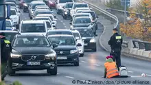 Eine Demonstrantin der Gruppe Letzte Generation sitzt, neben einem Polizeibeamten, auf der Ausfahrt der Stadtautobahn am Sachsenring. Die Aktivisten versuchten erneut an verschiedenen Stellen Blockaden zu errichten. Allerdings mit wenig Erfolg. So verhinderten Polizeibeamte am Sachsendamm und auch am Tempelhofer Damm, dass sich Aktivisten in großer Zahl auf den Straßen festkleben konnten. Nur vereinzelt erreichten die Aktivisten ihr Ziel. +++ dpa-Bildfunk +++