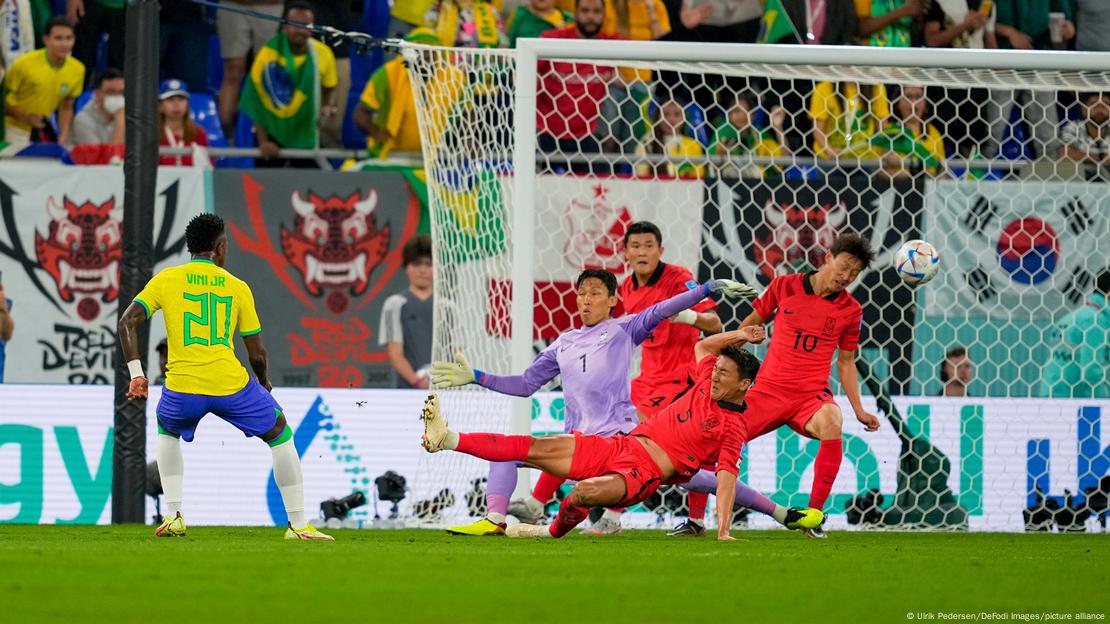Vinícius Jr. acerta um lindo chute colocado para marcar o seu primeiro gol em Copas do Mundo. Três defensores e o goleiro se jogam para tentar, em vão, impedir o gol.