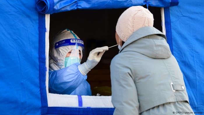 Eine Frau in Schutzkleidung nimmt mit Stäbchen Speichelprobe bei Frau