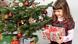 Child smiles, looking down at the present she is holding next to a Christmas tree. Child smiles, looking down at the present she is holding next to a Christmas tree.